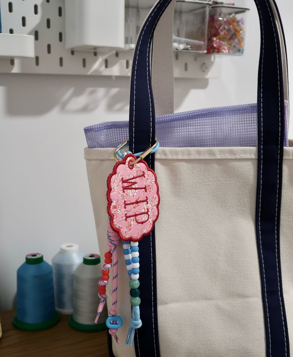 Pink scalloped WIP tag with a beaded hanger on a canvas tote